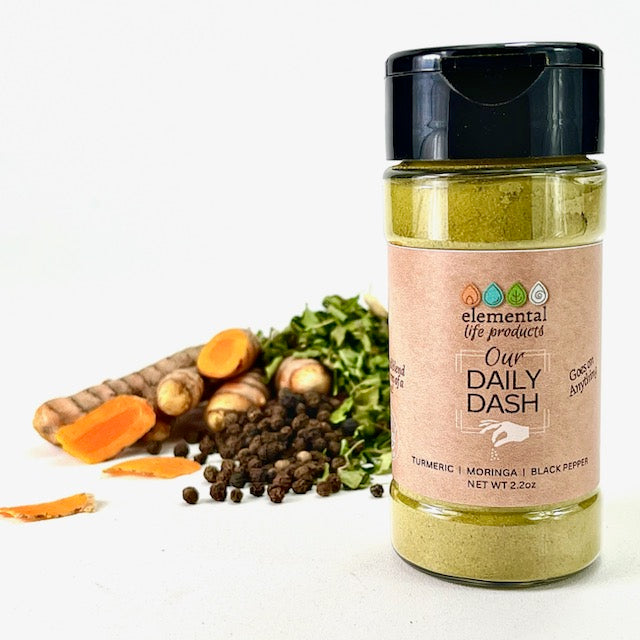 A container of Our Daily Dash with turmeric, black pepper and moringa raw ingredients in the background