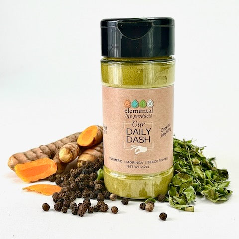 A container of Our Daily Dash surrounded by turmeric, black pepper and moringa raw ingredients