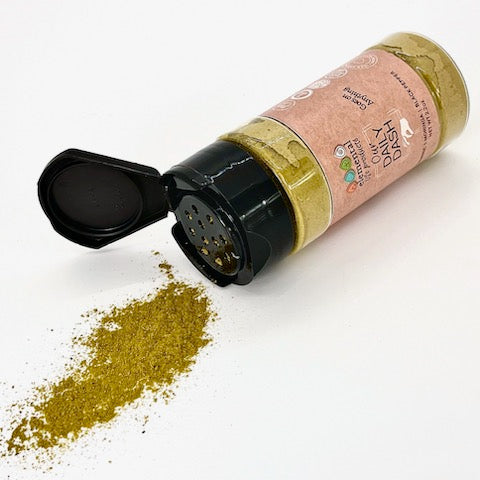 A container of Our Daily Dash laid over with fine seasoning mix poured onto a white background