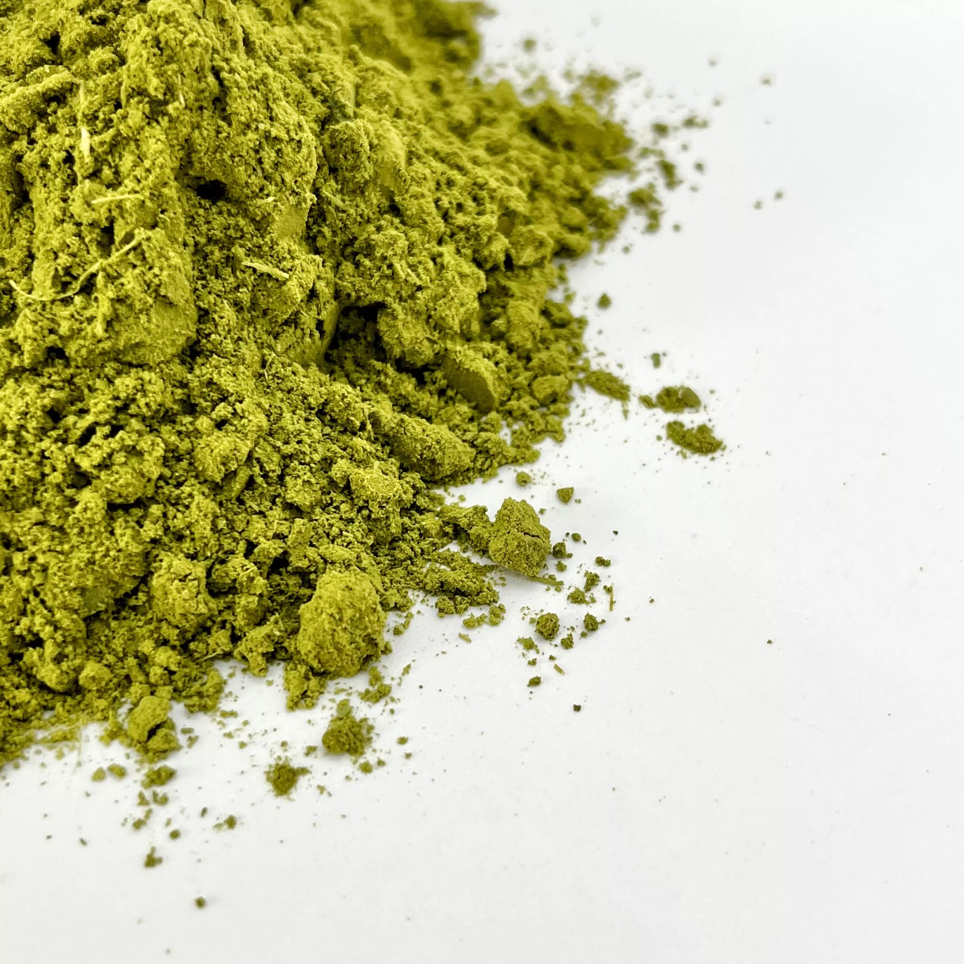 A pile of moringa powder in the corner of a white background